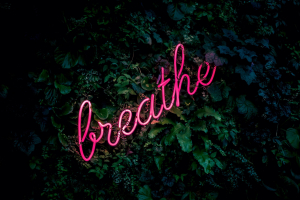 Pink neon breathe sign against a leafy background
