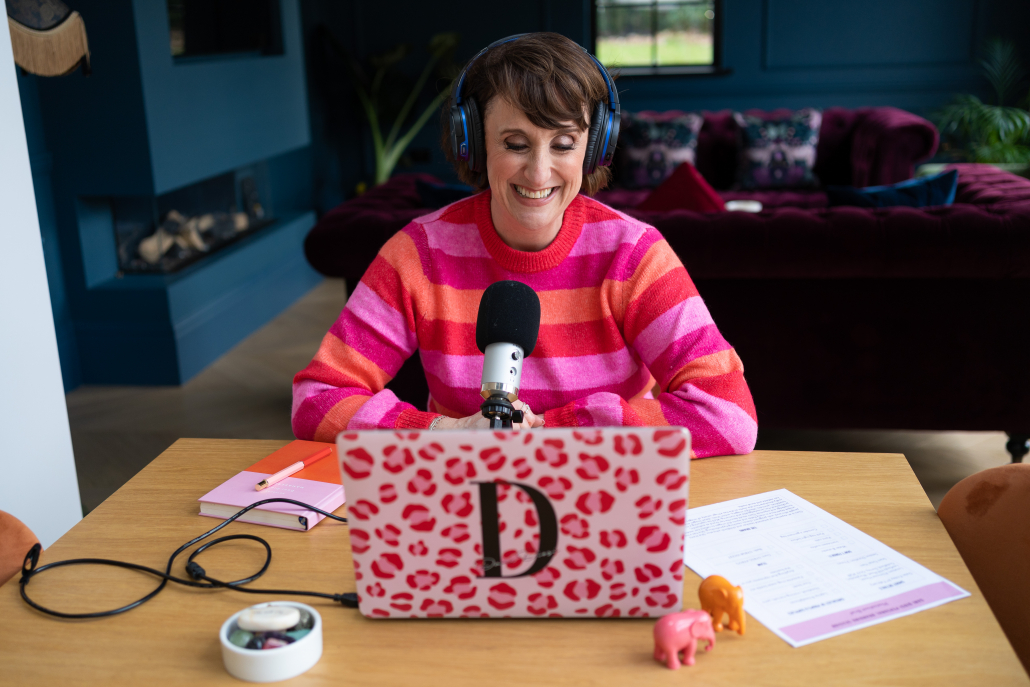 Dani Diosi wearing a brightly coloured top sitting at a table recording a hypnobirthing script for her hypnobirthing practitioner training