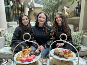 3 teenage girls sitting together on a couch having a cream tea on a day out with their mother Dani Diosi