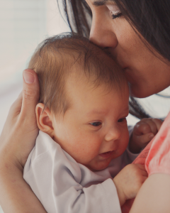 A mother cradles heer young baby against her shoulder. She is kissing it on it's head