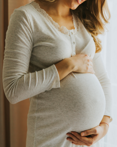 A pregnant woman dressed in a grey top cradles her pregnant bump in her hands. You can't see her head in the picture just the bump