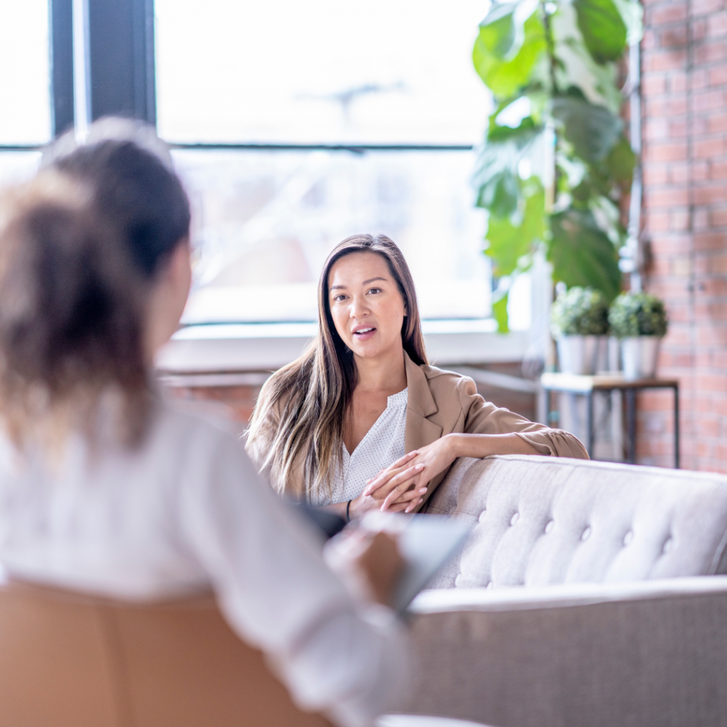 a woman in a brown cardigan sits on a sofa talking to her three step rewind practitioner who is helping with her birth truama